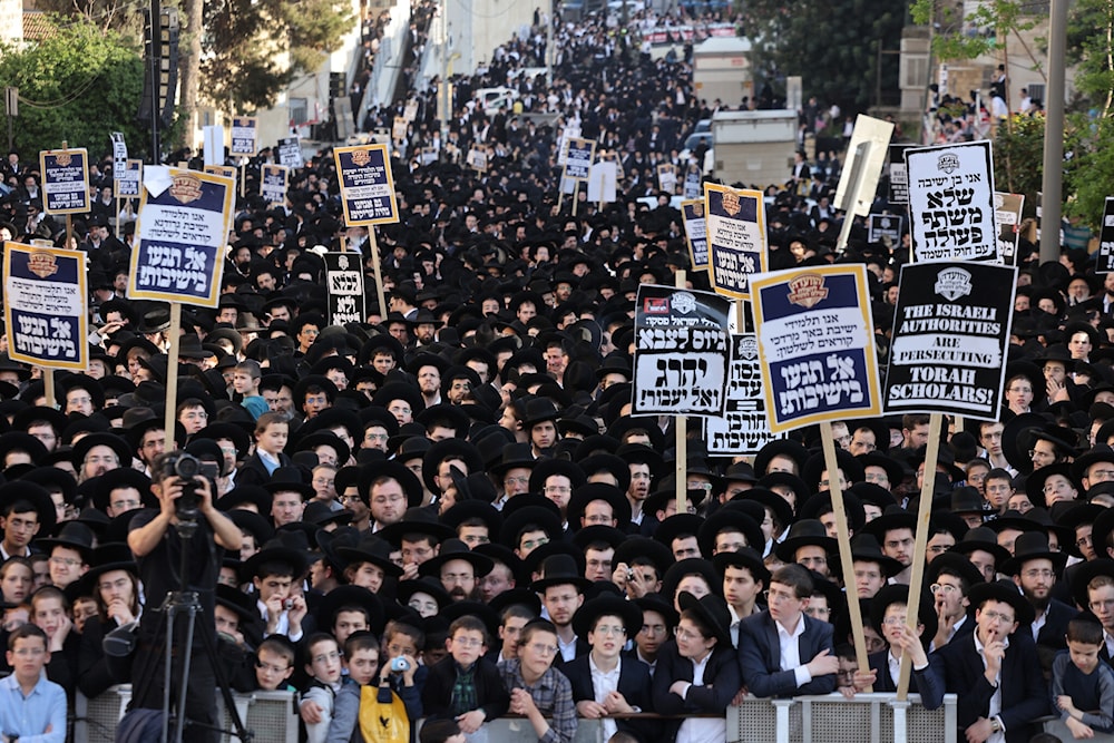Ultra-Orthodox Jewish men and youth raise placards during a protest against Israeli army conscription outside an army recruitment office in al-Quds on April 11, 2024. (AFP)
