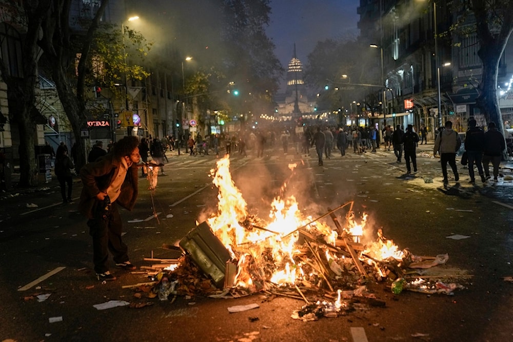 A man lights a cigarette from trash set alight by anti-government protesters outside Congress, where lawmakers debate a reform bill promoted by Argentine President Javier Milei in Buenos Aires, Argentina, Wednesday, June 12, 2024. (AP)