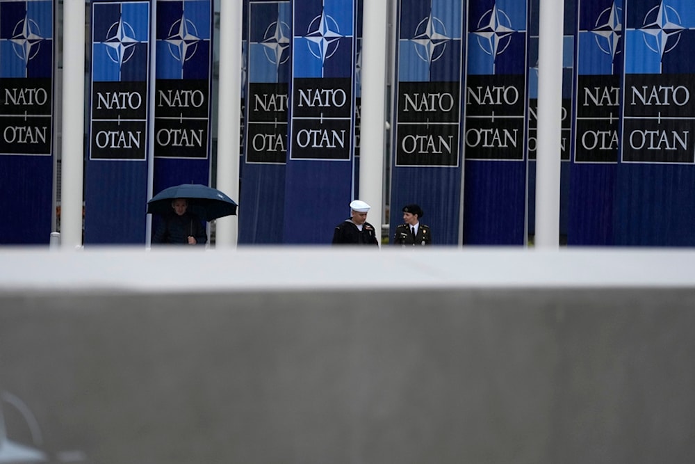 Two military personnel walk by NATO banners prior to a wreath laying ceremony at NATO headquarters in Brussels, Thursday, April 4, 2024. (AP)