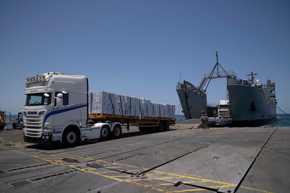 US Army soldiers stand next to trucks arriving loaded with humanitarian aid at the US-built floating pier Trident before reaching the beach on the coast of the Gaza Strip, occupied Palestine, June 25, 2024 (AP)