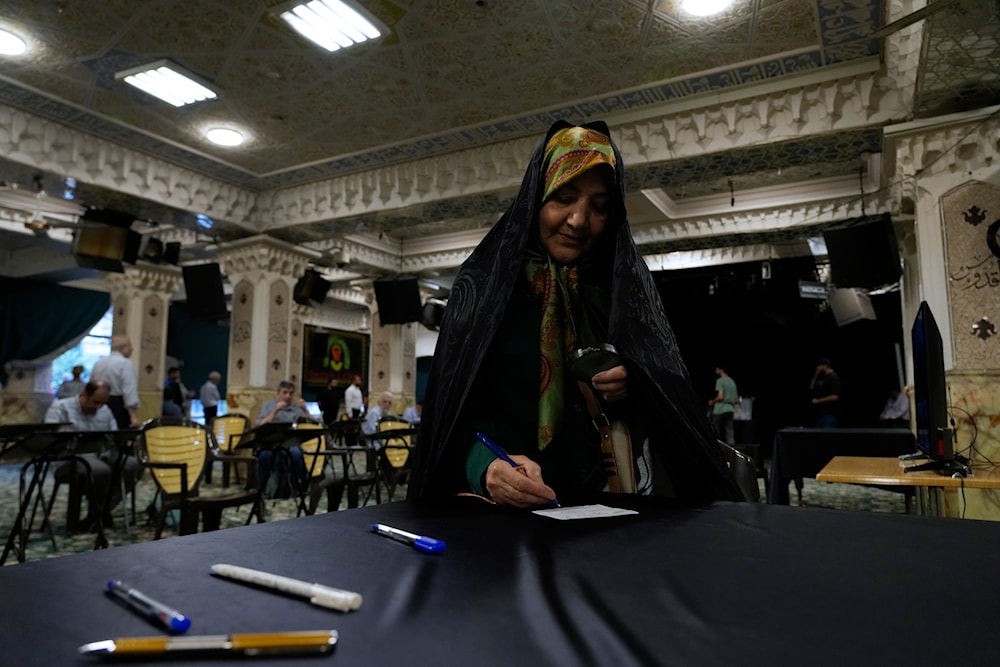 An elderly woman uses a magnifying glass to fill out her ballot for the presidential election at a polling station in Tehran, Iran, June 28, 2024 (AP)