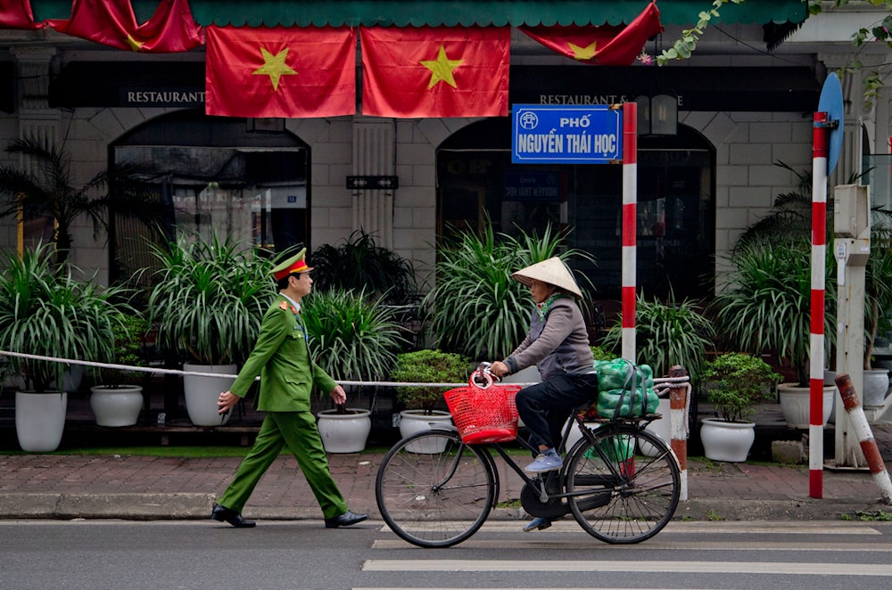 A woman rides a bicycle as a policeman walks past Vietnam flags in Hanoi, Vietnam, on February 27, 2019. (AP)