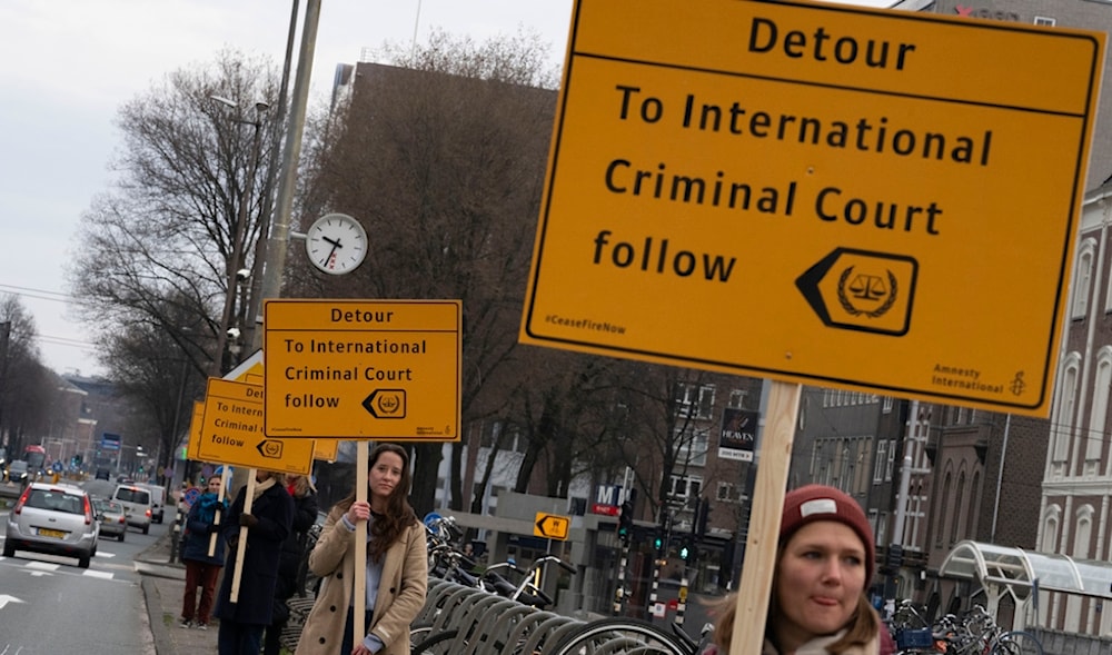 Amnesty International protesters hold signs pointing to the International Criminal Court along the route to the opening of a new National Holocaust Museum in Amsterdam, Netherlands, on March 10, 2024. (AP)