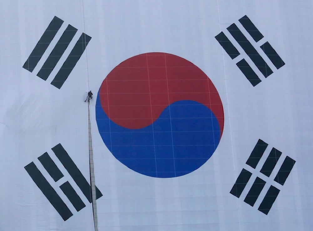 A worker hangs on a rope to adjust a national flag on the government complex building in Seoul, South Korea, Monday, Feb. 25, 2019. (AP)