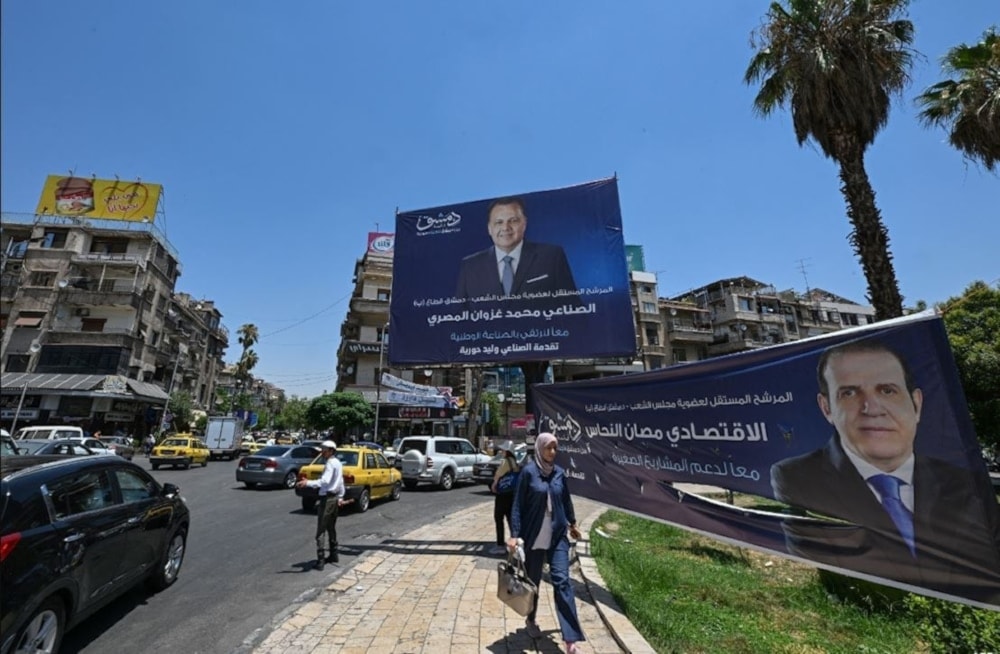 People walk past electoral campaign posters ahead of parliament elections in Damascus, Syria, on July 10, 2024. (AFP)