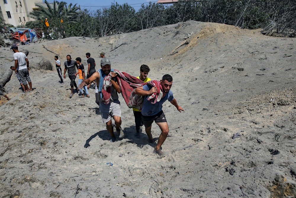 Palestinians evacuate a person killed by the Israeli occupation forces from a site hit by an Israeli bombardment on Khan Younis, southern Gaza Strip, July 13, 2024 (AP)