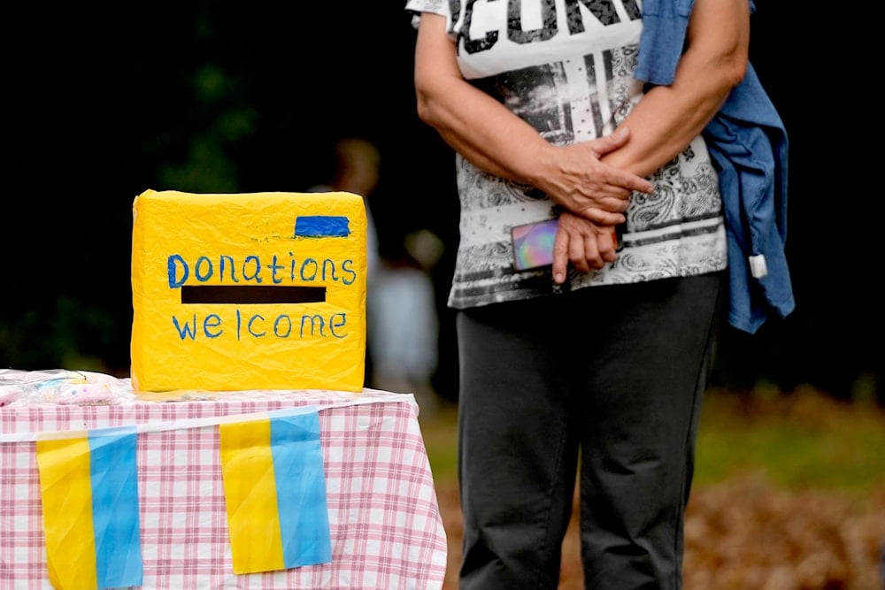 A woman waits near a donation box at the celebration for the Ukraine Independence day at a celebration in Chichester, south England, Saturday, Aug. 27, 2022.(AP)