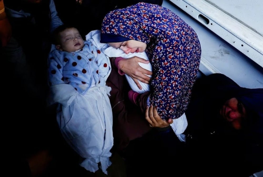 A Palestinian mother Rania Abu Anza's holds one of her five-month-old twins who were killed alongside her husband, and 11 other relatives in an Israeli airstrike. (@hamdahsalhut)