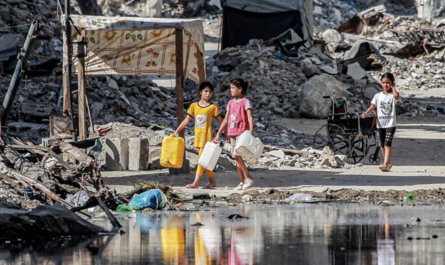 Palestinian girls walk past a lake of sewage leaking from targeted underground pipes by Israeli bombardment in Gaza's second city of Khan Younis amid the ongoing genocide (AFP)