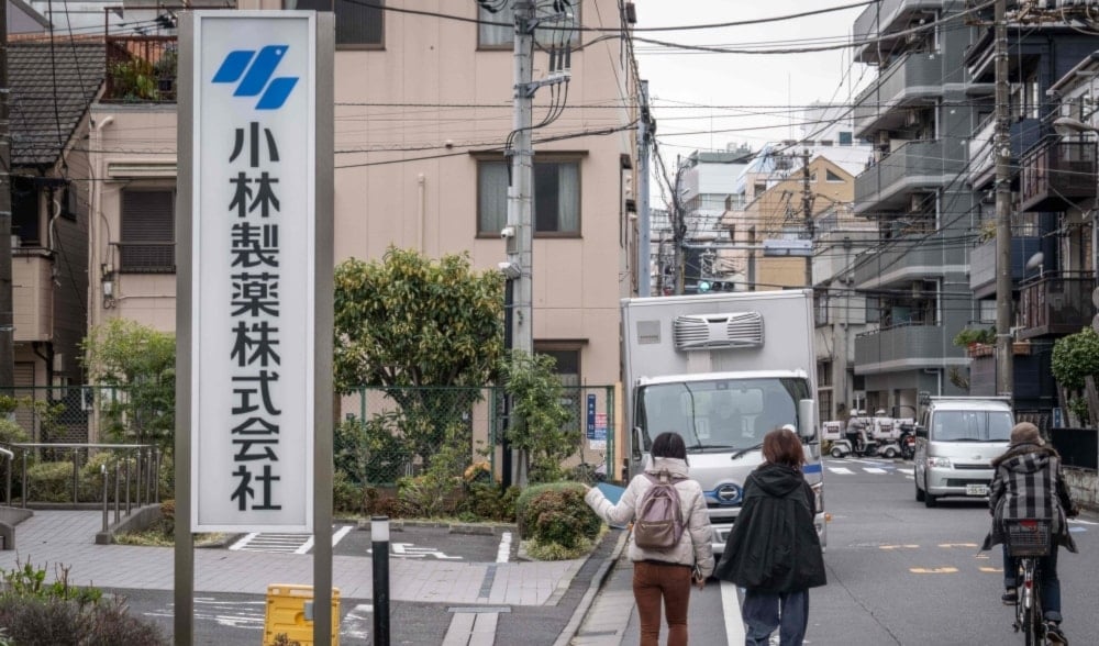 A woman points her finger at the signage of Kobayashi Pharmaceutical as she walks past the company's office in Tokyo on March 28, 2024. (AFP)