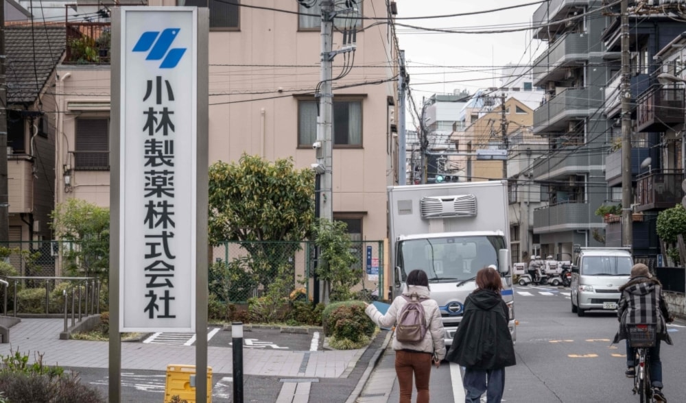 2024年3月28日、東京にある小林薬局のオフィスの前を通り過ぎる女性が、小林薬局の看板を指差す。  （AFP）