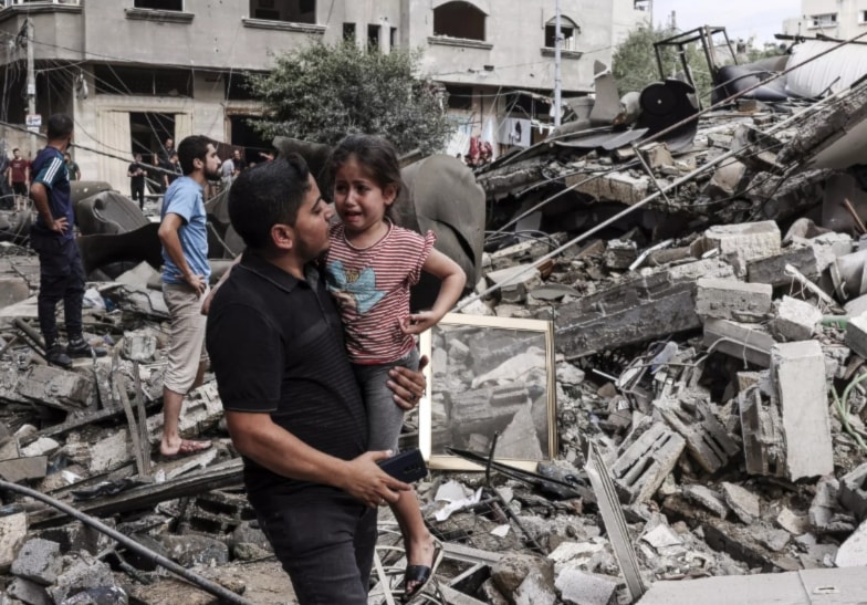 A Palestinian father carries his crying son as he walks in front of a building destroyed in an Israeli air strike in Gaza City on October 7, 2023. (AFP)