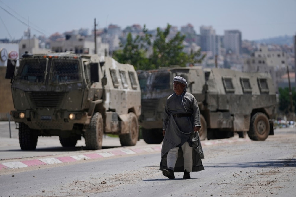 A Palestinian man walks past two Israeli military personal carriers during an Israeli raid on the occupied west bank refugee camp of Tulkarm, on Tuesday, July 23,202. (AP)