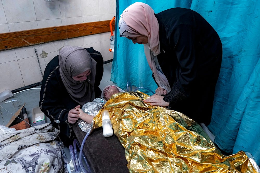 Amal Abdel-Hadi, left, and Nour Abdel-Hadi, right, react over their 2-year-old wounded niece, Siwar, as she receives treatment at a hospital in Deir al-Balah, on July 24, 2024. (AP)