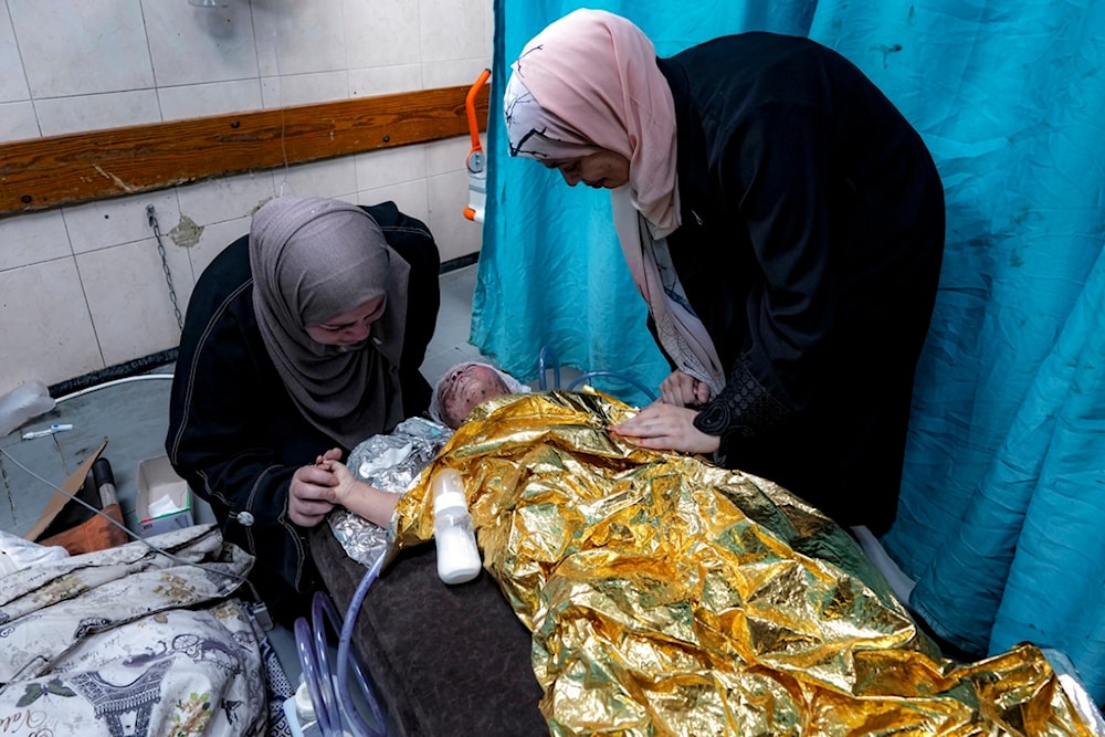 Amal Abdel-Hadi, left, and Nour Abdel-Hadi, right, react over their 2-year-old wounded niece, Siwar, as she receives treatment at a hospital in Deir al-Balah, Wednesday, July 24, 2024. (AP)