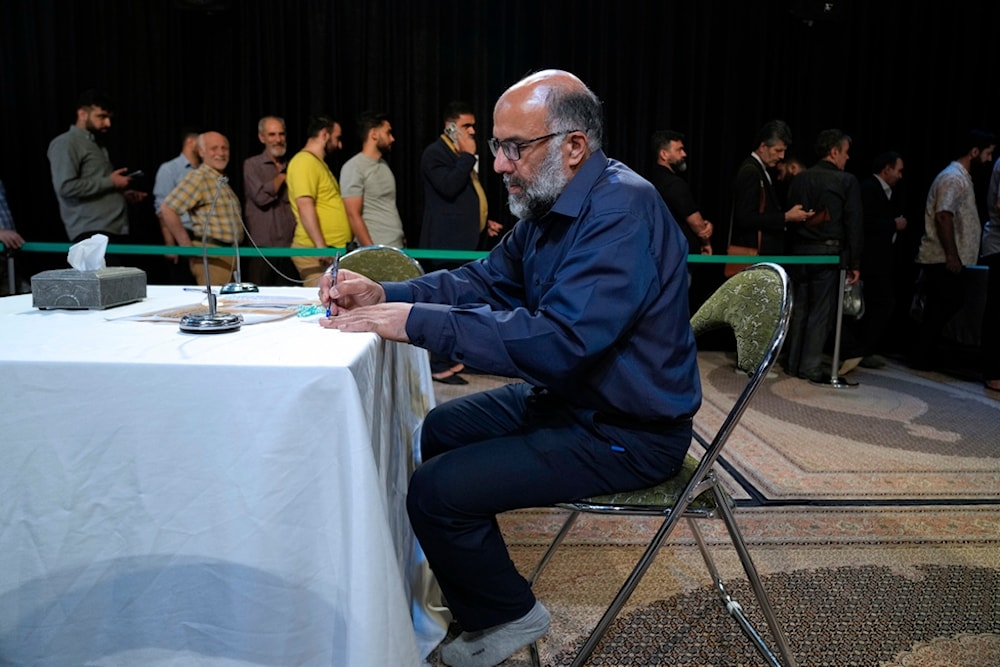 A man fills out his ballot as others line up during the presidential election in a polling station at the shrine of Saint Saleh in northern Tehran, Iran, Friday, July 5, 2024. (AP)