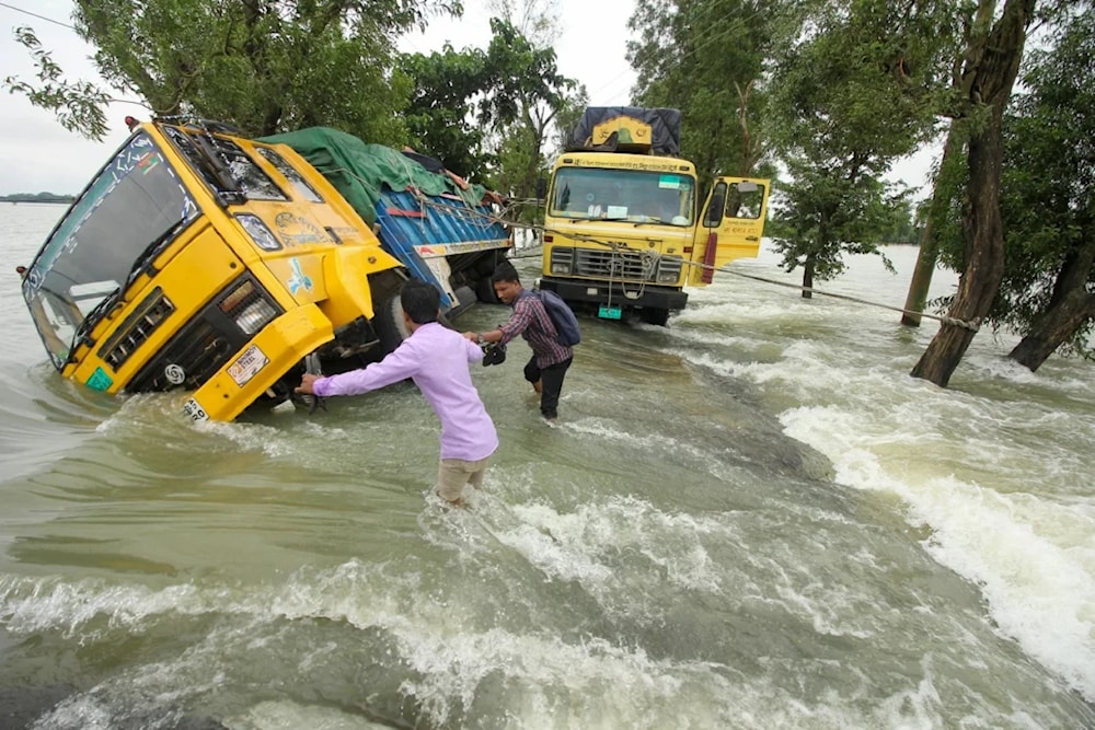 People wade past stranded trucks on a flooded street in Sunamganj, Bangladesh on June 21, 2022. (AFP)