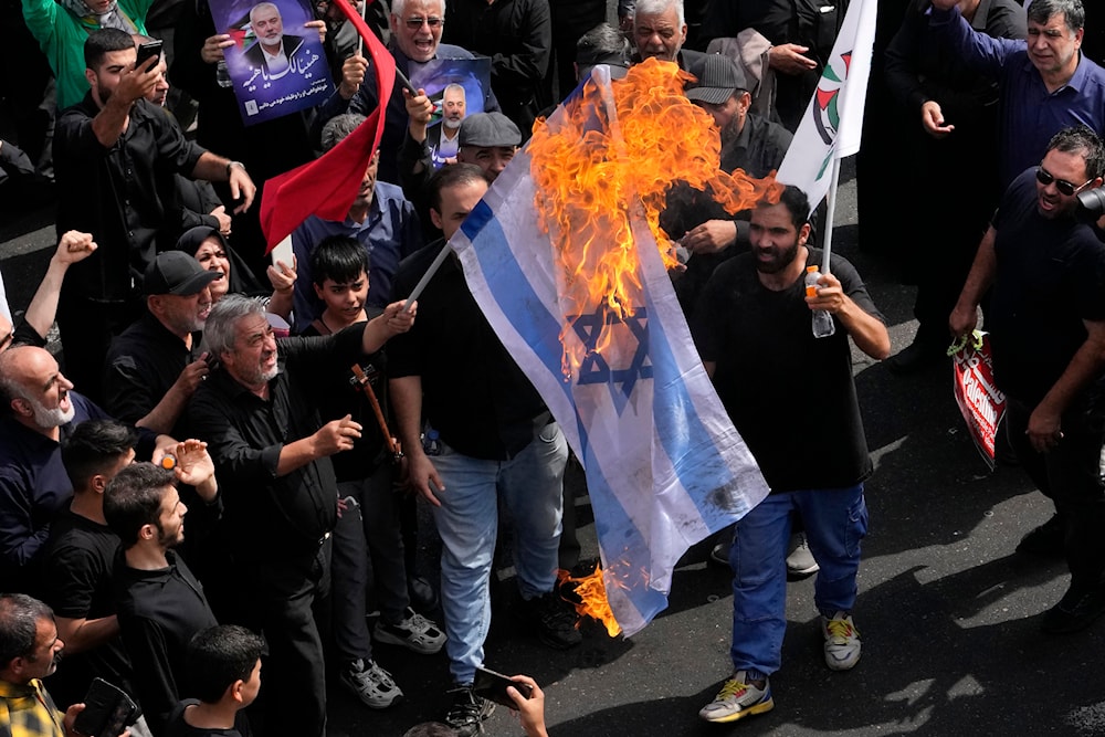 Iranians burn a representation of the Israeli flag during the funeral ceremony of Hamas leader Ismail Haniyeh and his bodyguard who were killed in an Israeli airstrike at Enqelab-e-Eslami Sq. in Tehran, Iran, Thursday, August 1, 2024 (AP)