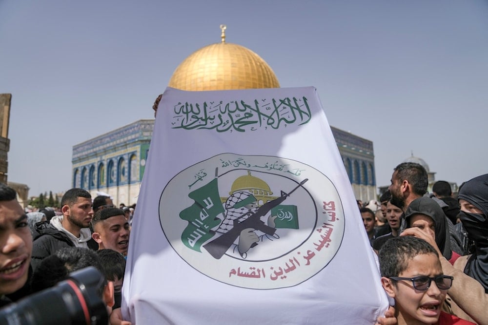 Palestinians hold a sign with the Izz ad-Din al Qassam Brigades logo outside the Al-Aqsa Mosque compound during the holy month of Ramadan, in al-Quds' Old City, March 24, 2023. (AP)