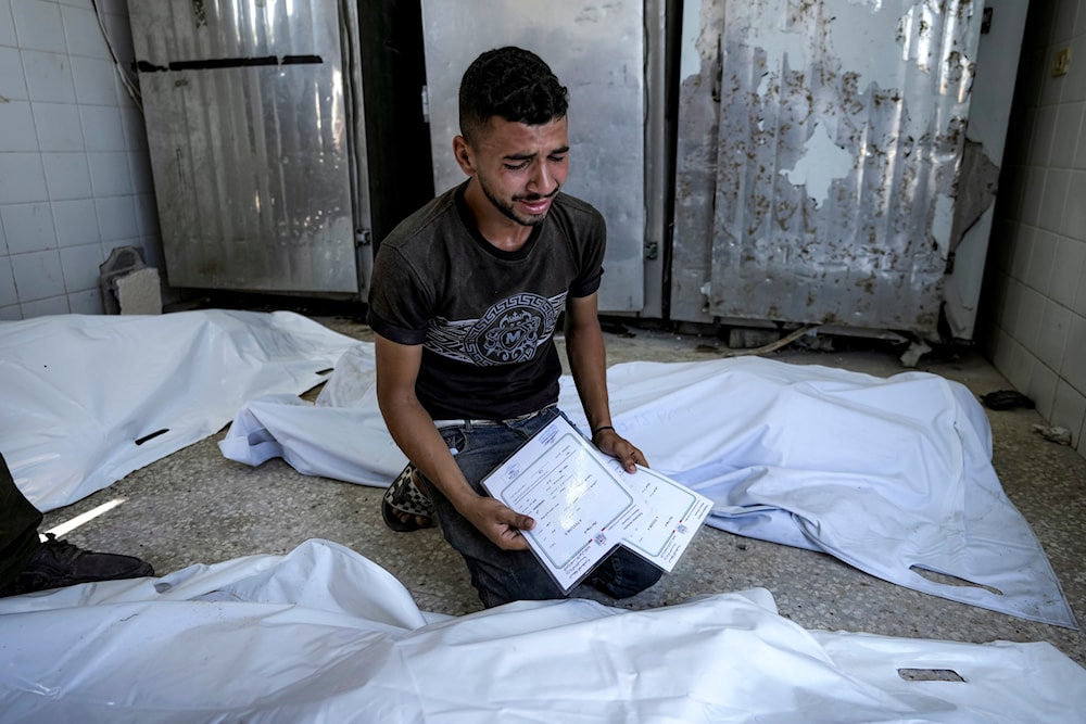 A Palestinian man mourns his 4-day-old twin relatives, killed in the Israeli bombardment of the Gaza Strip, as he holds their birth certificates, at a morgue in Deir al-Balah, Aug. 13, 2024. (AP)