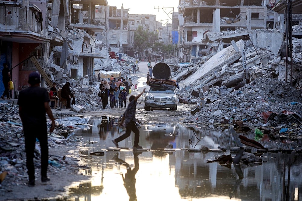 Palestinians displaced by the Israeli air and ground offensive on the Gaza Strip, walk past sewage flowing into the streets of the southern town of Khan Younis, Gaza Strip, July 4, 2024 (AP)