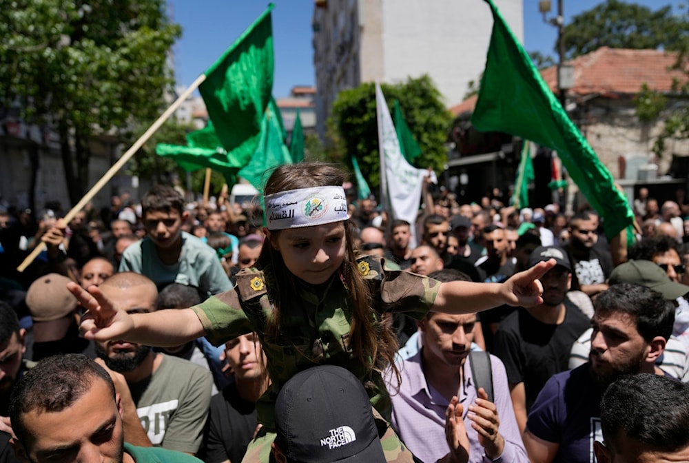 A Palestinian man carries a girl with a headband that reads the al-Qassam Brigades, as they protest the assassination of leader Ismail Haniyeh, in the West Bank city of Ramallah, July 31, 2024. (AP)