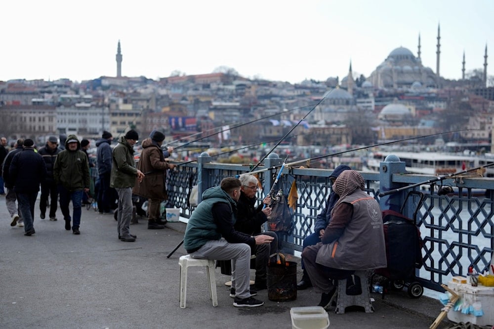 People warm themselves with a fire while fishing over the Galata bridge in Istanbul, Turkey, Wednesday, Feb. 21, 2024. (AP)