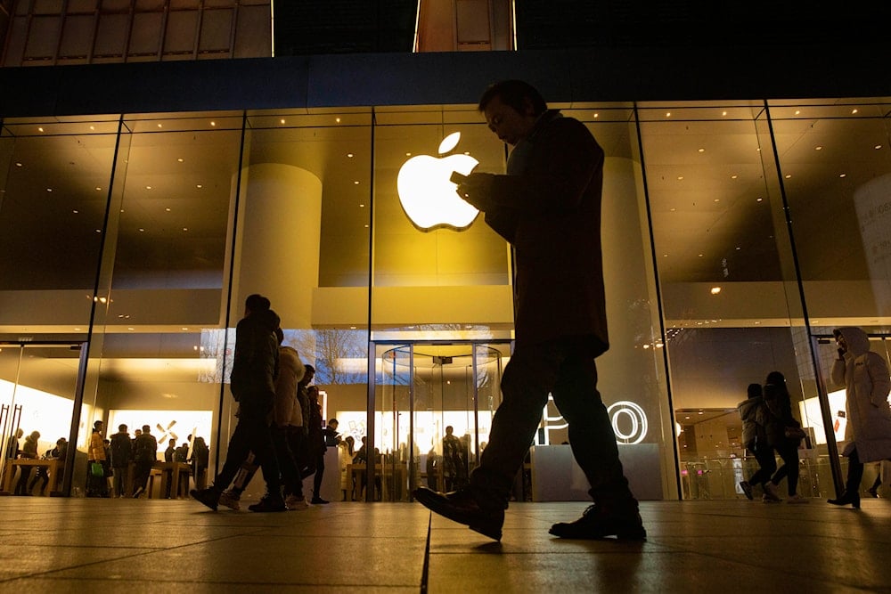 file photo, a man looks at his phone as he walks past a store of U.S. tech giant Apple in a retail district in Beijing on December 13, 2024