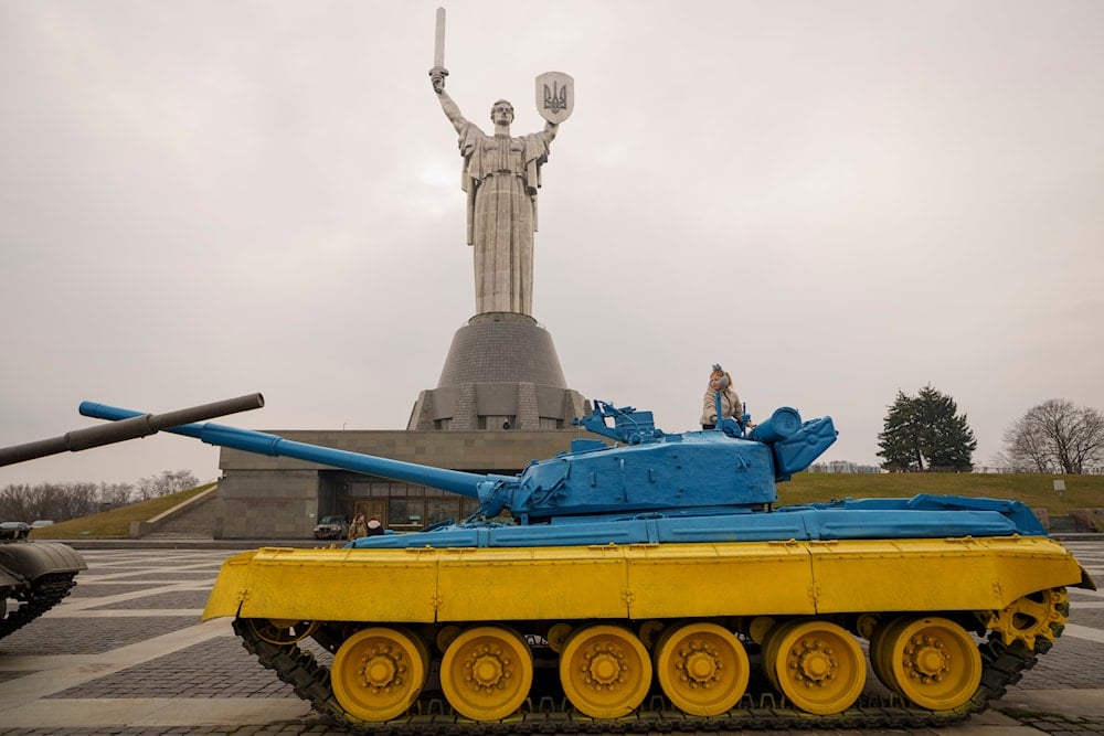 A child plays on a tank painted in the colors of the Ukrainian flag, back dropped by the Motherland Monument, in Kyiv, Ukraine, Friday, March 15, 2024. (AP)