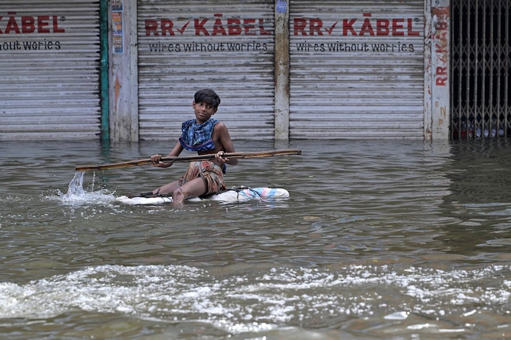 A young boy uses a bamboo to steer himself floating on a log of wood through a flooded street in Feni, a coastal district in southeast Bangladesh, Saturday, Aug. 24, 2024. (AP)