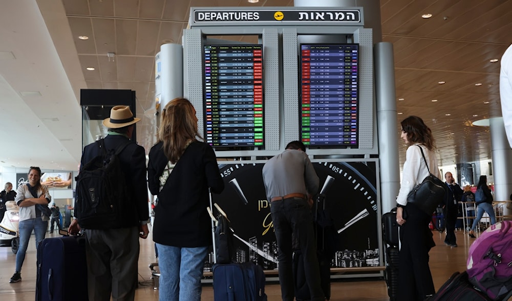 Israeli settlers and passengers look at the monitor displaying delayed flights at Ben Gurion airport, near Tel Aviv, occupied Palestine, Monday, March 27, 2023. (AP)