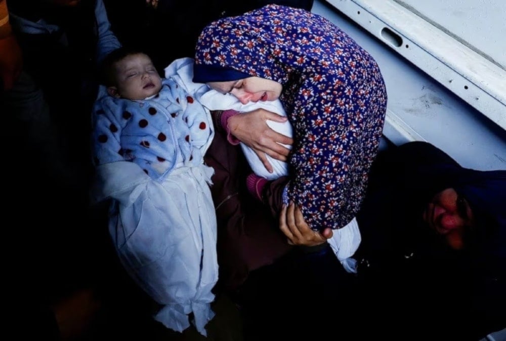 A Palestinian mother Rania Abu Anza holds one of her five-month-old twins who were killed alongside her husband and 11 other relatives in an Israeli airstrike. (@hamdahsalhut)