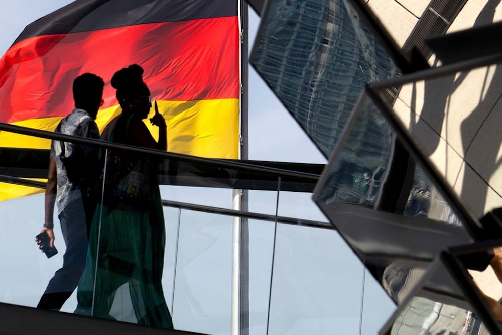 Two people walk in front of a German national flag as they visit the dome of the Reichstag building, home of the German federal parliament, Bundestag, in Berlin, Germany, September 1, 2024 (AP) 