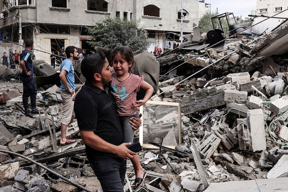 A Palestinian father carries his traumatized child as he walks in front of a residential building destroyed in an Israeli airstrike on Gaza city on October 7,2023. (AFP)