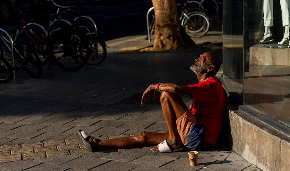 An Israeli settler sits on the sidewalk next to a mall in Tel Aviv, occupied Palestine, Thursday, Aug. 15, 2024. (AP)