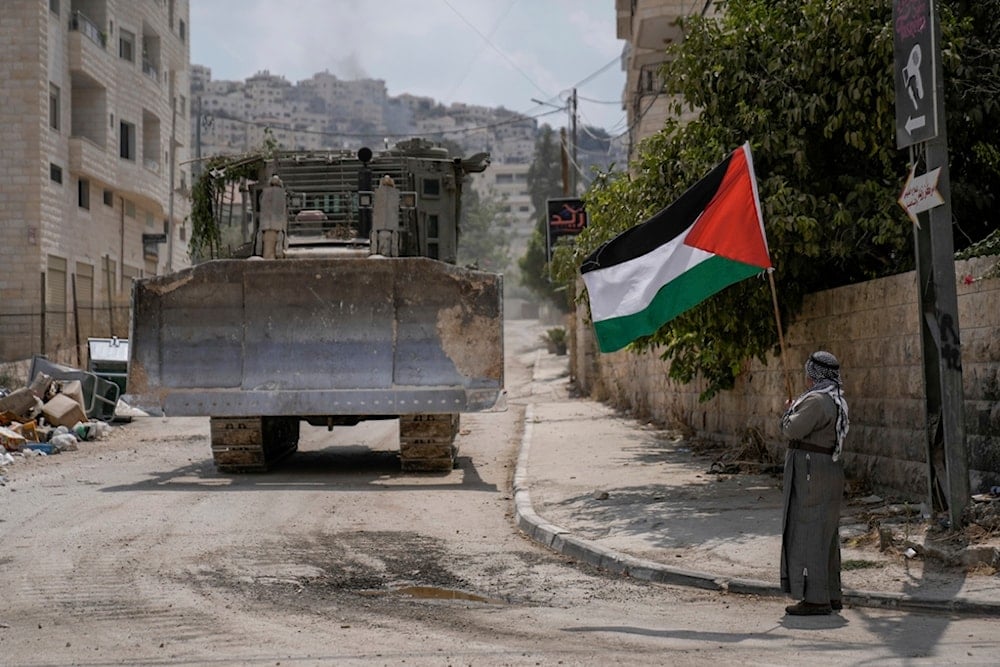 A man waves the Palestinian flag as a convoy of Israeli military bulldozers drive by during an occupation raid in Jenin, West Bank, Monday, Sept. 2, 2024. (AP)