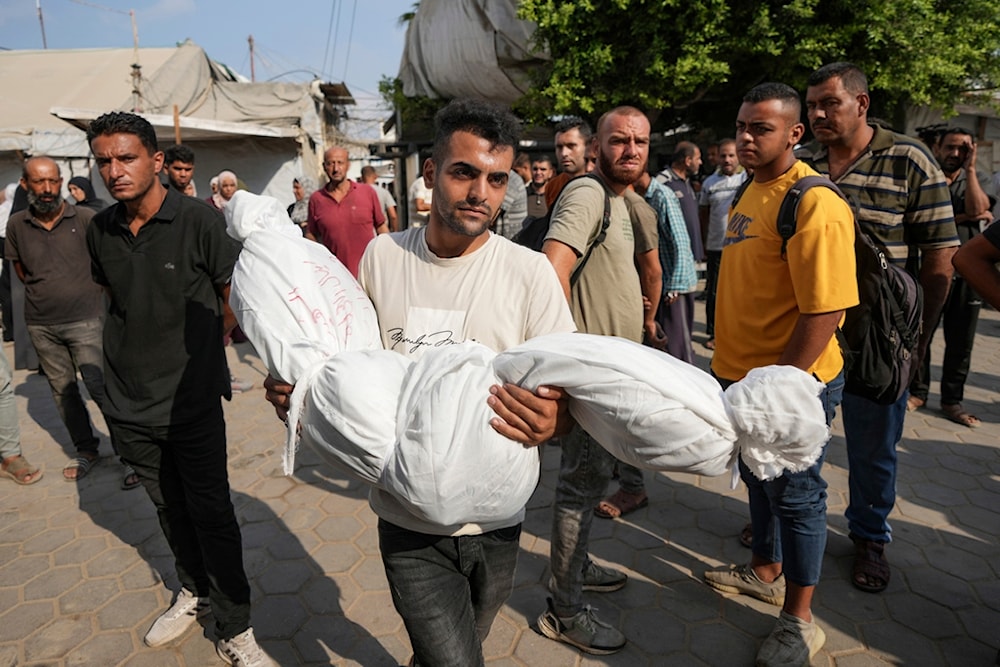 A Palestinian carries a body at the funeral for more than 15 people, including several children and women, killed in an Israeli strike, at al-Aqsa Martyrs Hospital in Deir al-Balah, Gaza Strip, August 17, 2024 (AP)