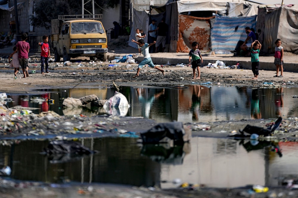 Displaced children walk through a dark streak of sewage flowing into the streets of Deir al-Balah, central Gaza Strip, August 29, 2024 (AP)