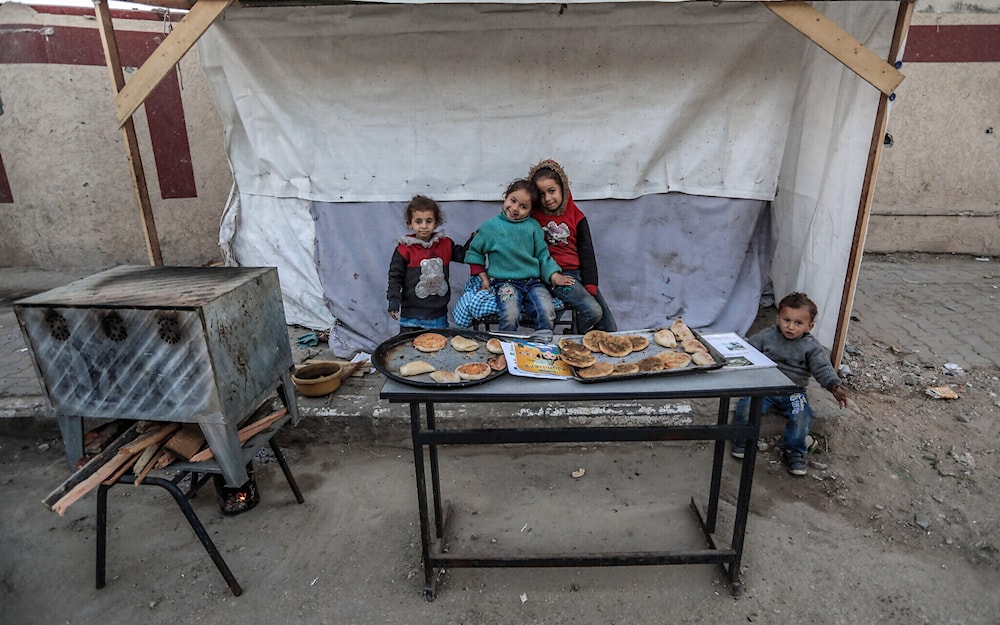 Palestinian Children pose for a picture at a stand selling flatbread in Deir al-Balah in central Gaza on March 3, 2024 amid Israeli genocide. (AFP)