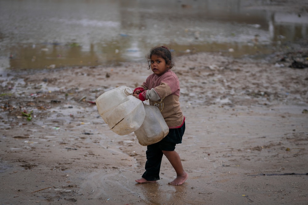 A young girl walks barefoot, carrying empty jerrycans to collect water, after overnight rainfall at the refugee tent camp for displaced Palestinians in Deir al-Balah, central Gaza Strip, on December 31, 2024. (AP)