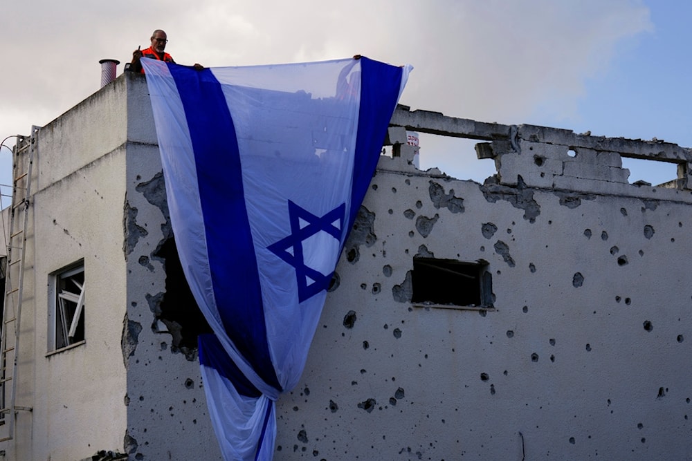 Municipality workers hang an Israeli flag over a damaged building that was hit by a rocket fired from Lebanon, in Kiryat Bialik, northern occupied Palestine, on Sunday, September 22, 2024 (AP)