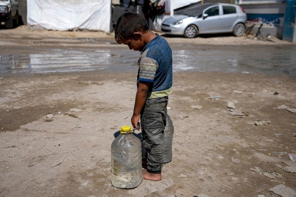 A displaced child carries filled water bottles at a makeshift tent camp in Deir al-Balah, central Gaza Strip, Thursday, August 29, 2024. (AP)