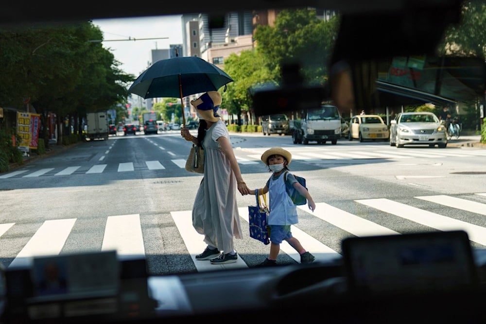 A pedestrian crossing a street with a child is seen through a taxi window in Tokyo, Monday, July 19, 2021 (AP Photo/David Goldman, File)