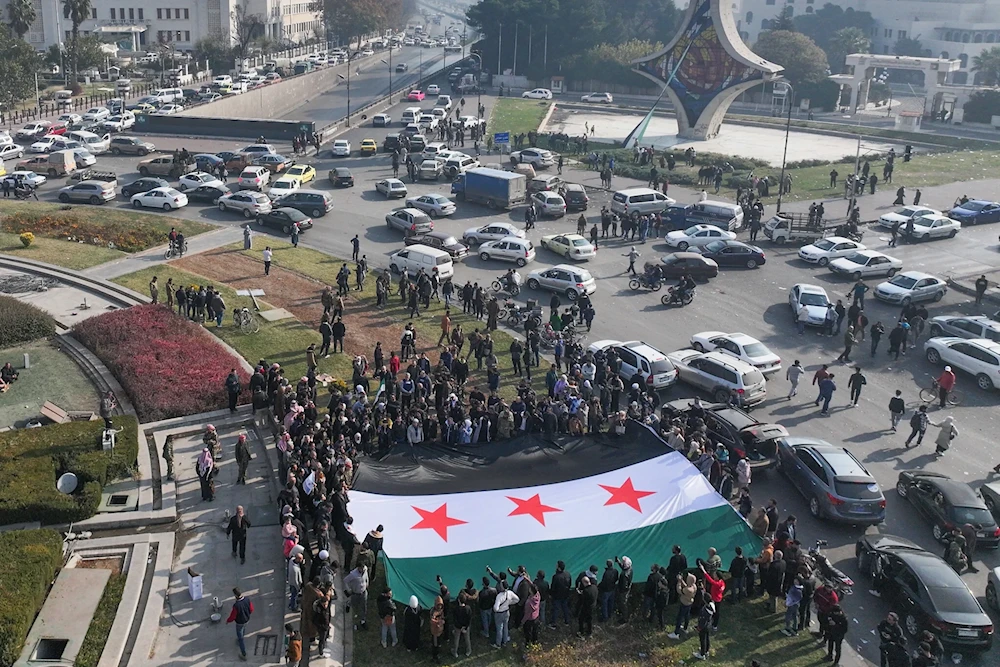 People celebrate holding a large Syrian opposition flag at Umayyad Square in Damascus on December 9, 2024. (AFP)