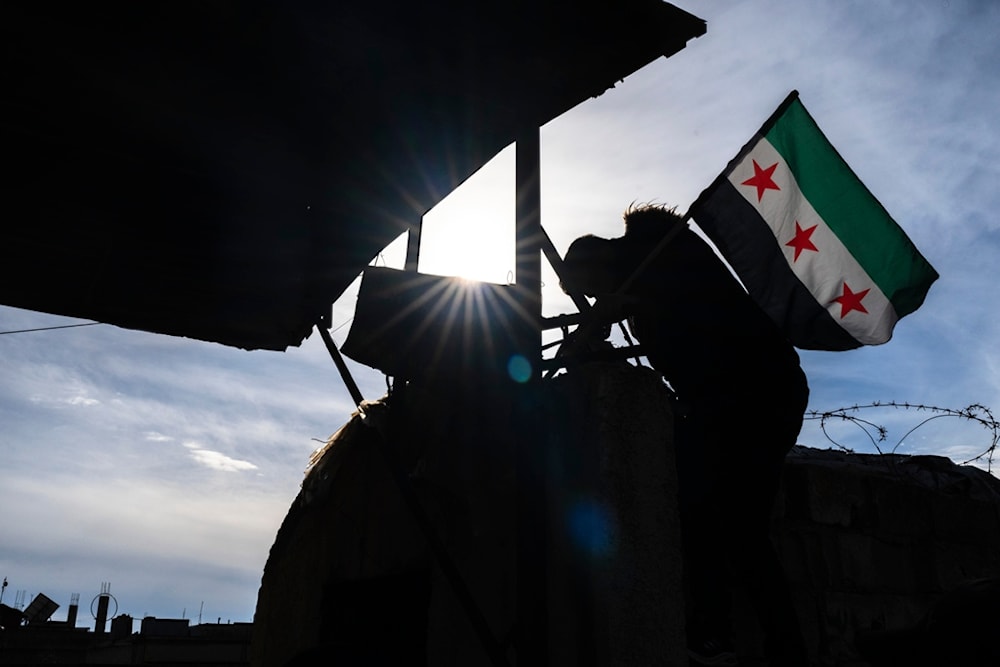 A man raises the new Syrian flag at a security building, in Nawa, near Daraa, Syria, Jan. 4, 2025. (AP Photo/Mosa'ab Elshamy)