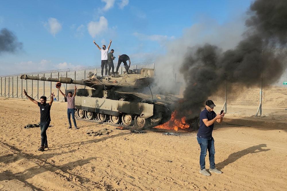 Palestinians celebrate by a destroyed Israeli tank at the Gaza Strip fence east of Khan Younis on October 7, 2023. (AP)