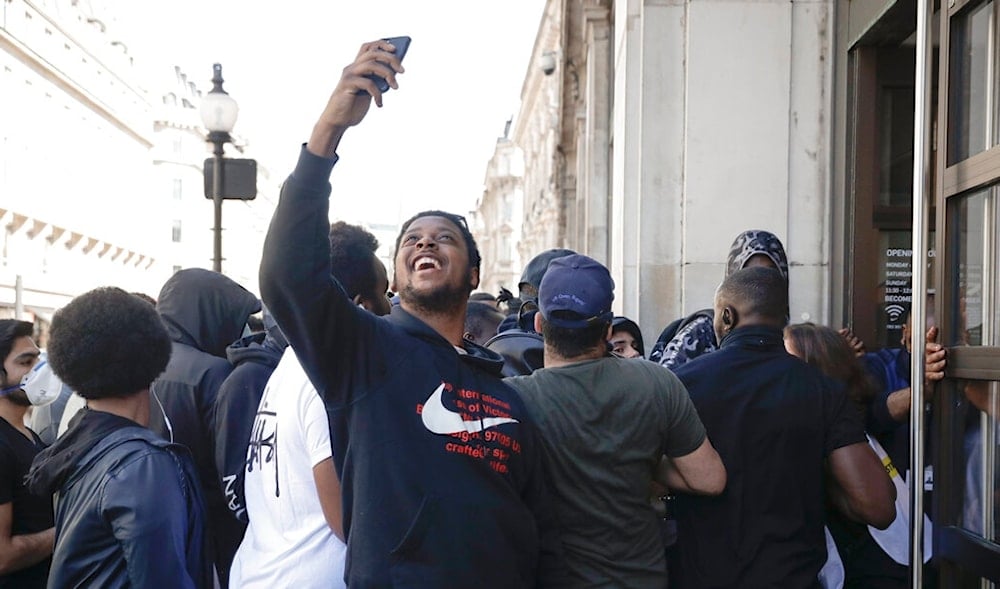 A youth takes pictures as people queueing push to enter the Niketown shop in London, Monday, June 15, 2020.  (AP)