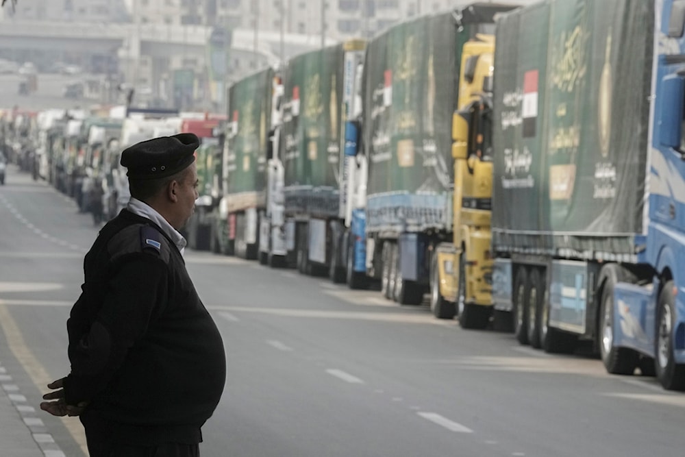 An Egyptian policeman stands in front of trucks of humanitarian aid at a parking point in Cairo, Egypt, as they wait to travel to cross the Rafah border crossing between Egypt and the Gaza Strip, Sunday, Jan. 26, 2025 (AP)