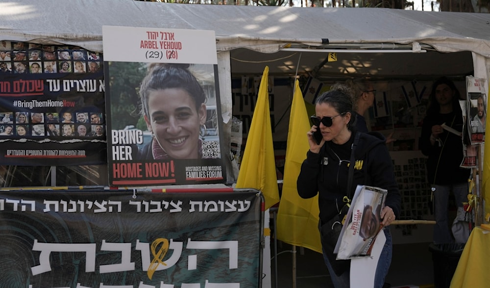 A woman walks past a photo of Arbel Yehud, and a banner in Hebrew calling for a prisoner-exchange with Hamas, at the entrance of a tent set up in occupied al-Quds, Monday, Jan. 27, 2025. (AP)