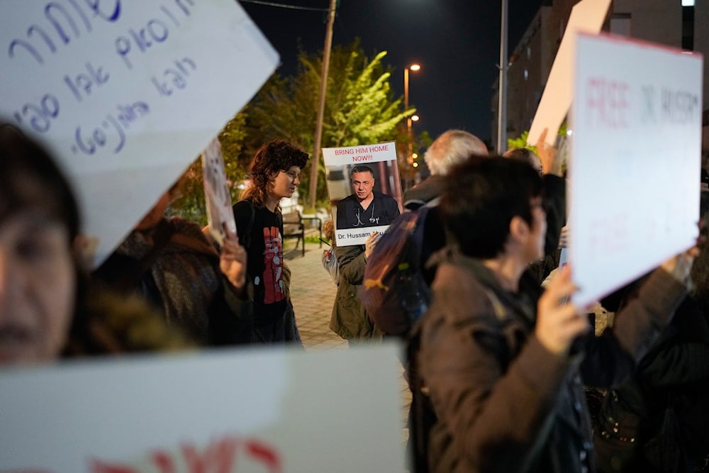 A woman holds a sign featuring a photo of Palestinian Dr. Hussam Abu Safiya during a protest in front of the Shin Bet offices, calling for his release, in 'Tel Aviv', occupied Palestine on January 1, 2025. (AP)